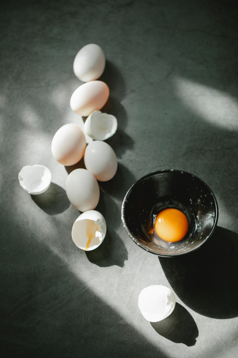 pile of eggs and shells scattered on table near bowl with raw yolk