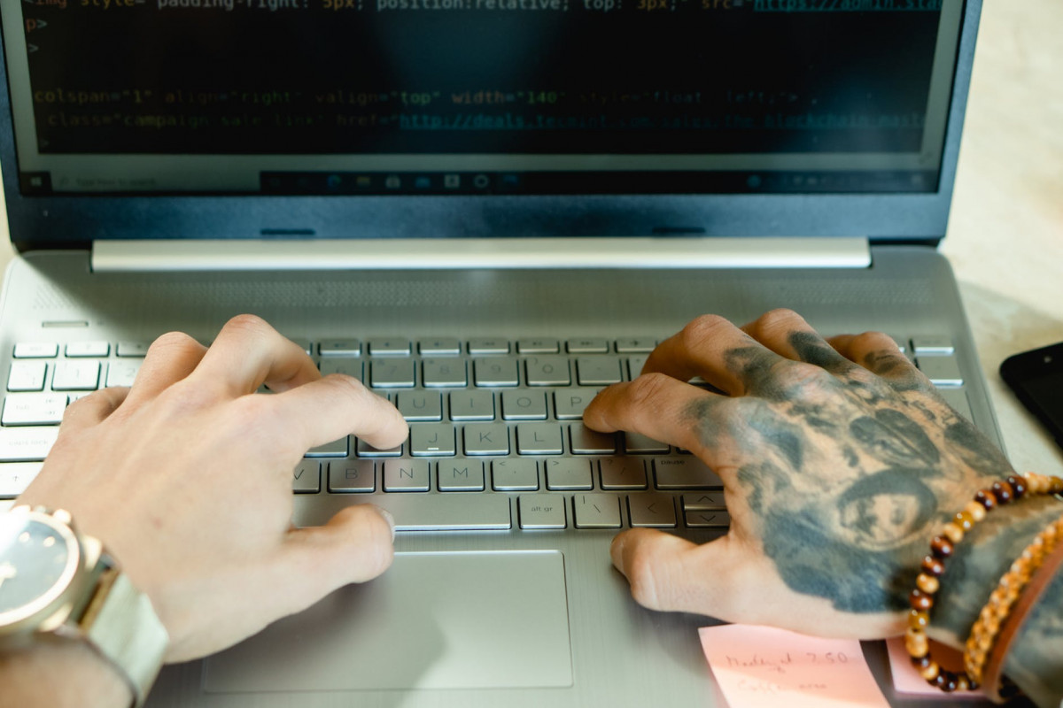 close up photo of a person with tattoos typing on a laptop keyboard