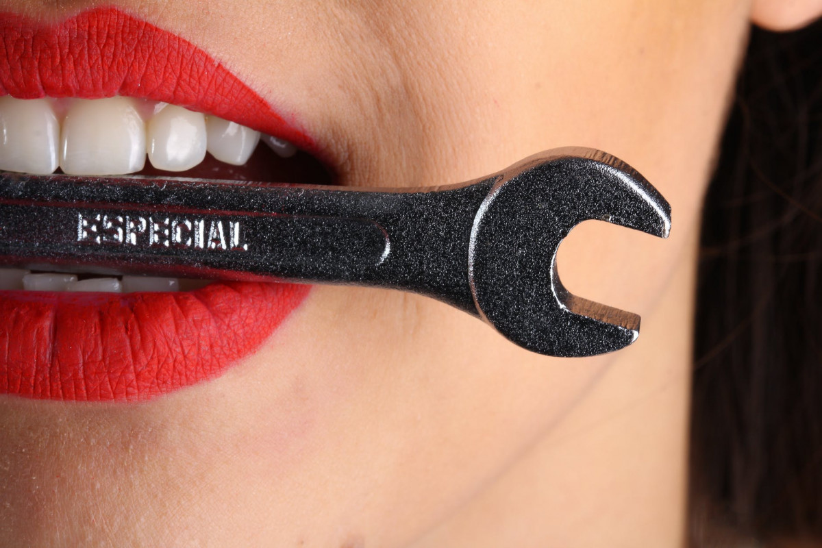 close view of woman with red lips biting gray special wrench