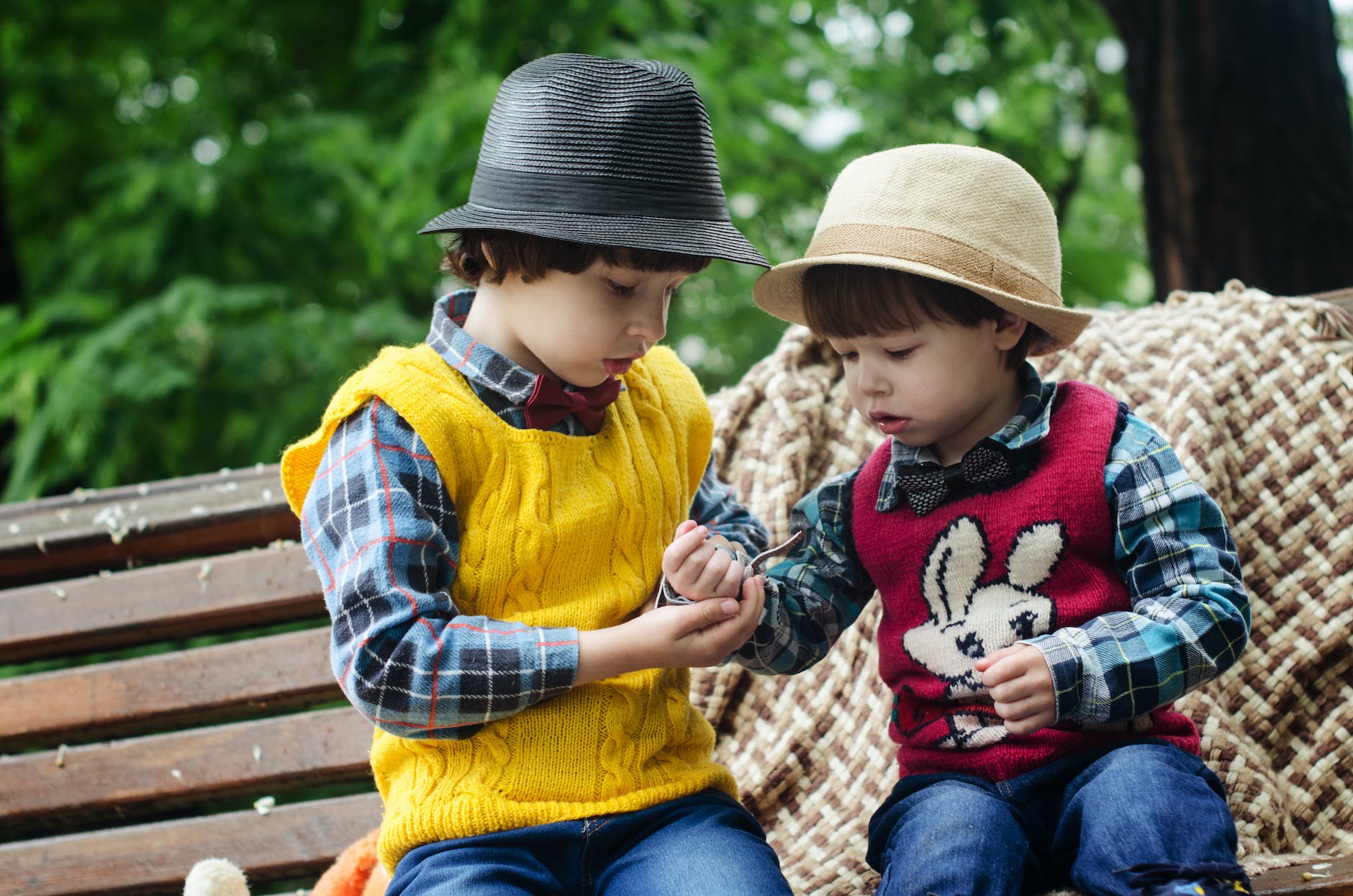two boys sitting on bench wearing hats and long sleeved shirts