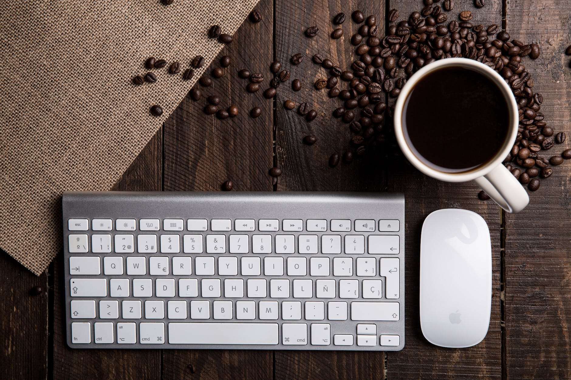 flat lay photography of apple magic keyboard mouse and mug filled with coffee beside beans
